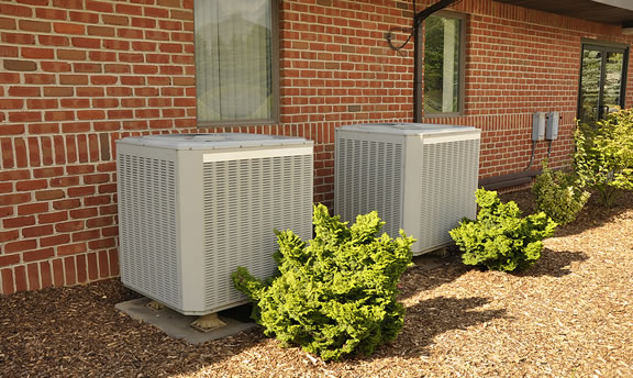 Two air conditioning units in Manchester, MO against a brick building.