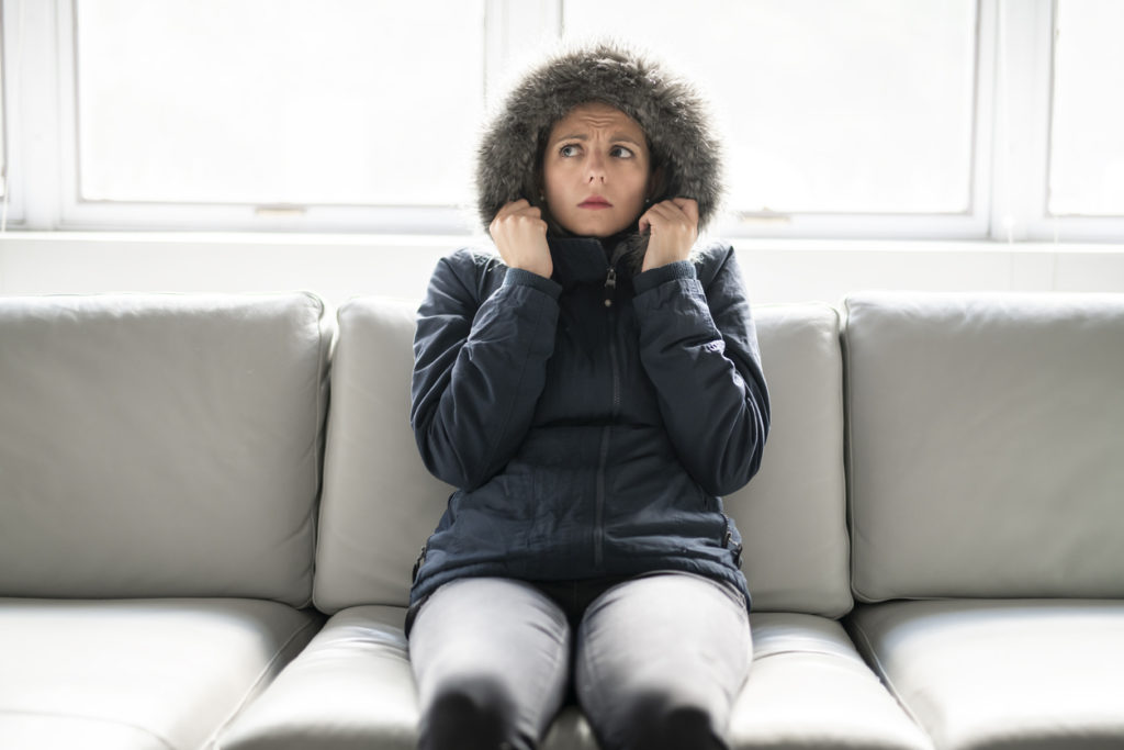 Cold woman in parka listening for furnace clicking sounds